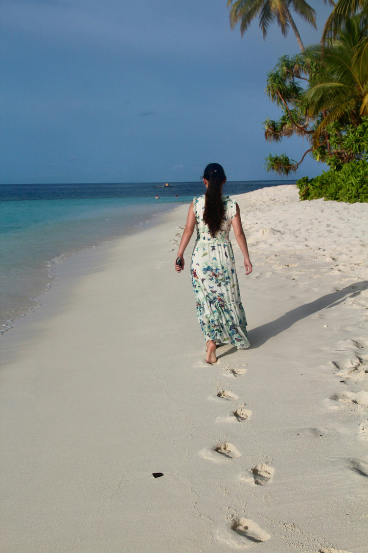 Outfit donna estate 2025: ragazza con abito leggero che cammina sulla spiaggia, look estivo elegante e fresco.