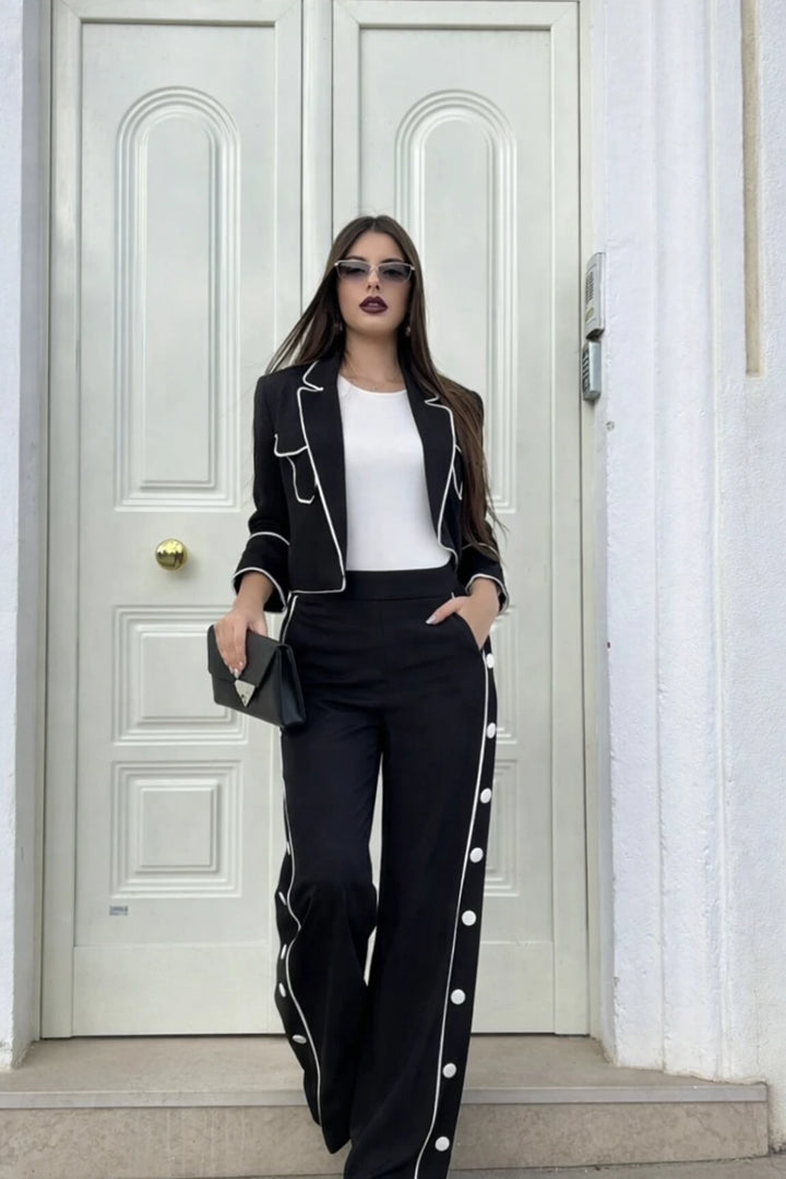 La modella indossa un completo nero con giacca e pantalone a palazzo con dei bottoni laterali in tendenza 